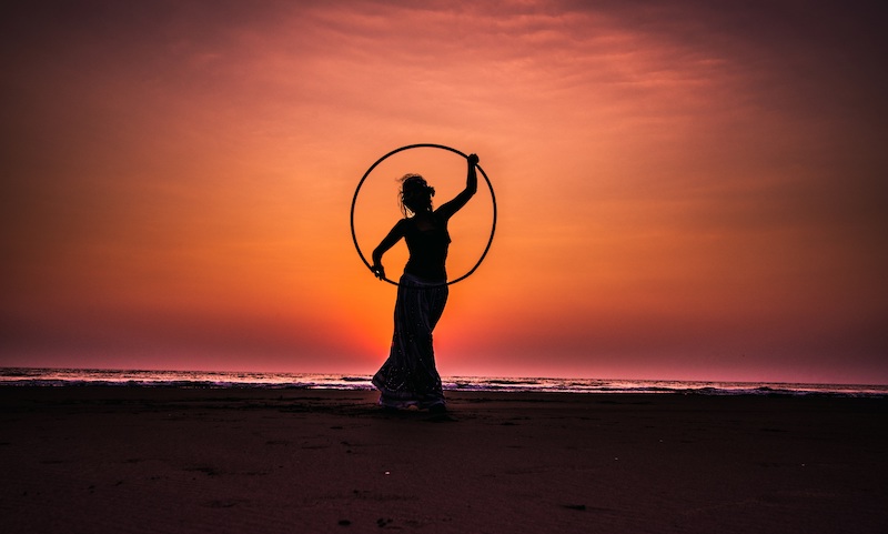 Frau mit Hula-Hoop-Reifen. Sonnenuntergang im Hintergrund.