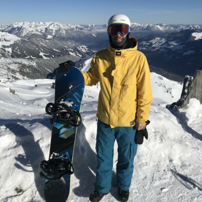 Mensch mit gelber Skijacke und Snowboard im Schnee