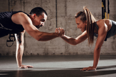 Fit And Strong Zwei Menschen schlagen die Hände ein während sie Planken machen.