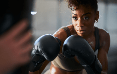 Eine Frau hat schwarze Boxhandschuhe an und ist beim Boxtraining