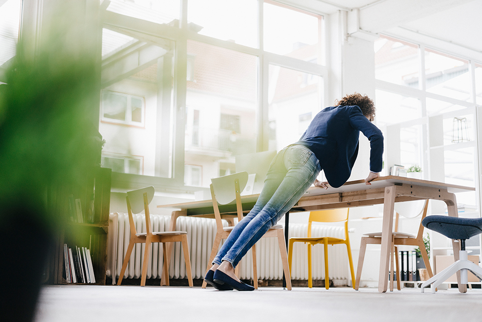 Geschäftsfrau im Büro macht Liegestütze auf dem Schreibtisch