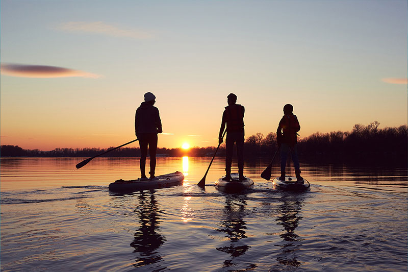 Drei Personen fahren SUP im Sonnenuntergang