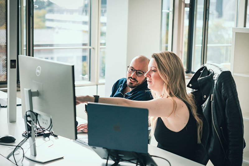 hansefit_unternehmen_office Ein Mann und eine Frau im Büro schauen auf einen Desktop und besprechen sich