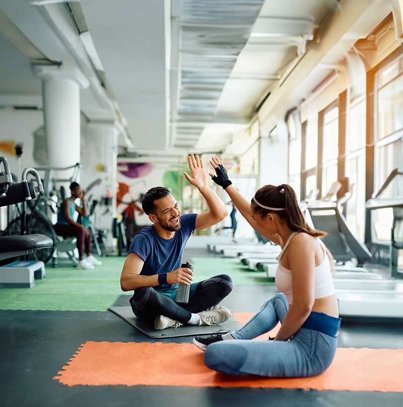 hansefit_unternehmen_yoga_fitness Ein Mann und eine Frau im Fitnessstudio sitzen auf Yogamatten und geben sich High Five