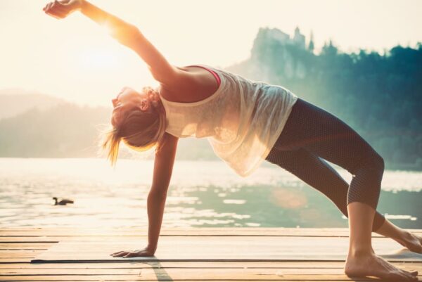 Eine Frau steht vor einem See und macht Yoga