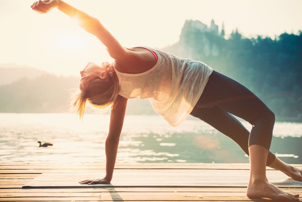 Eine Frau steht vor einem See und macht Yoga