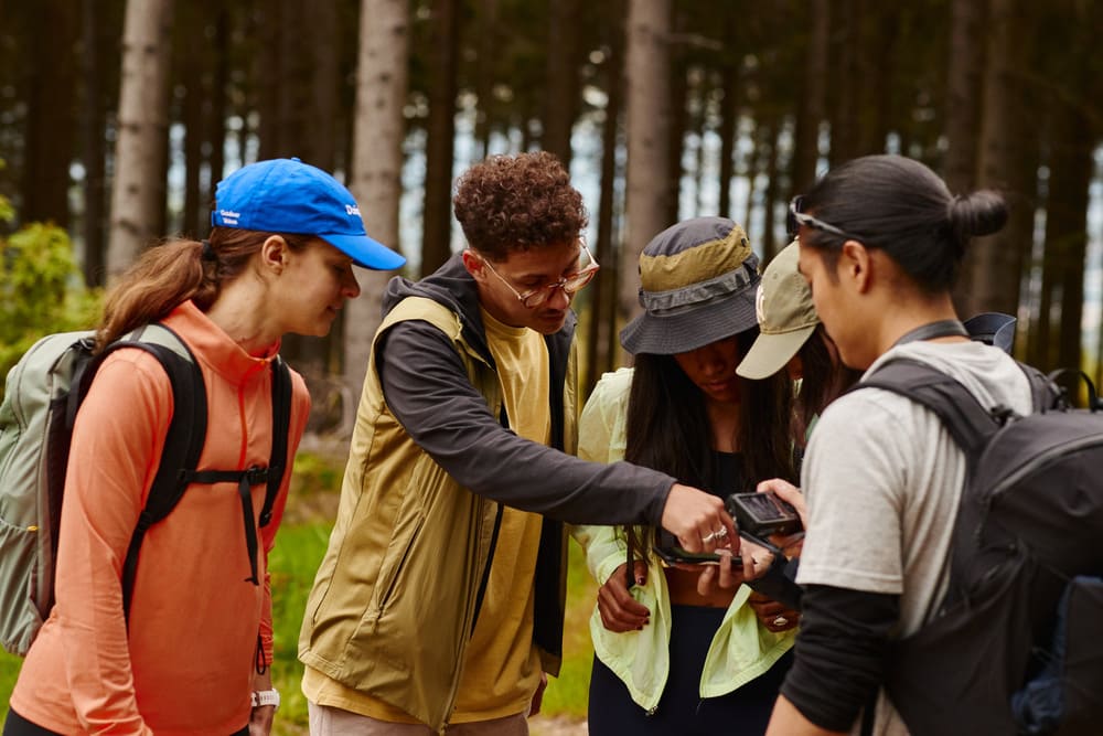 Das Bild zeigt 5 Personen im Walk in Wanderausstattung die zusammen auf ein Handy schauen.