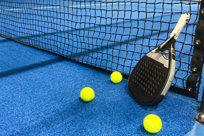 voll-bock-auf-padel-2 Ein Padelschläger and Netz gelehnt mit Bällen um ihn herum.