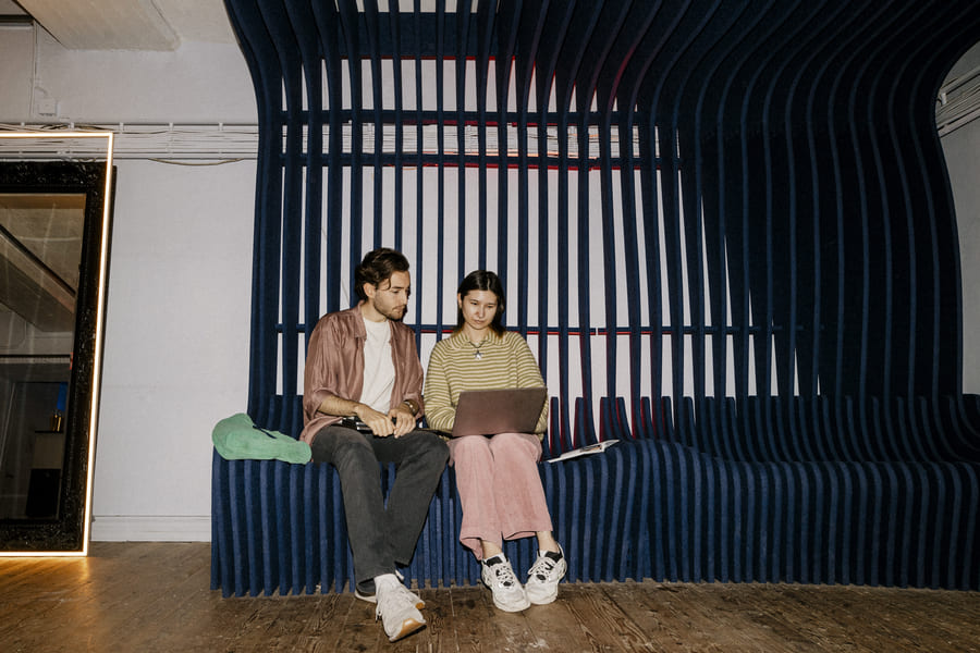 Zwei Mitarbeitende sitzen zusammen auf einer Bank im Büro und besprechen sich.