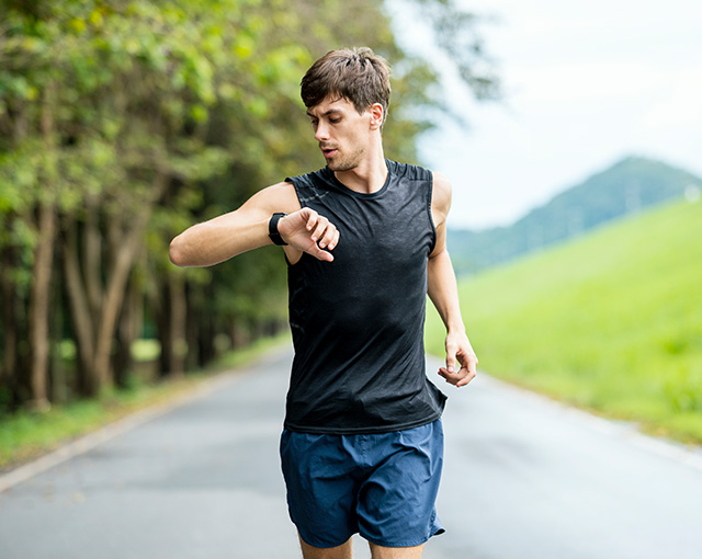 activity-rewards-einreichen Ein Mann läuft durch einen Park und schaut auf seine Smart Watch